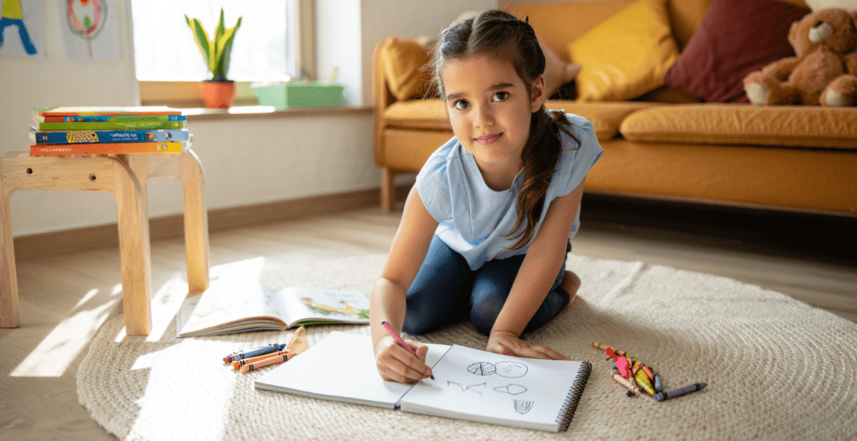 Child drawing with crayons on a rug, looking at the camera.